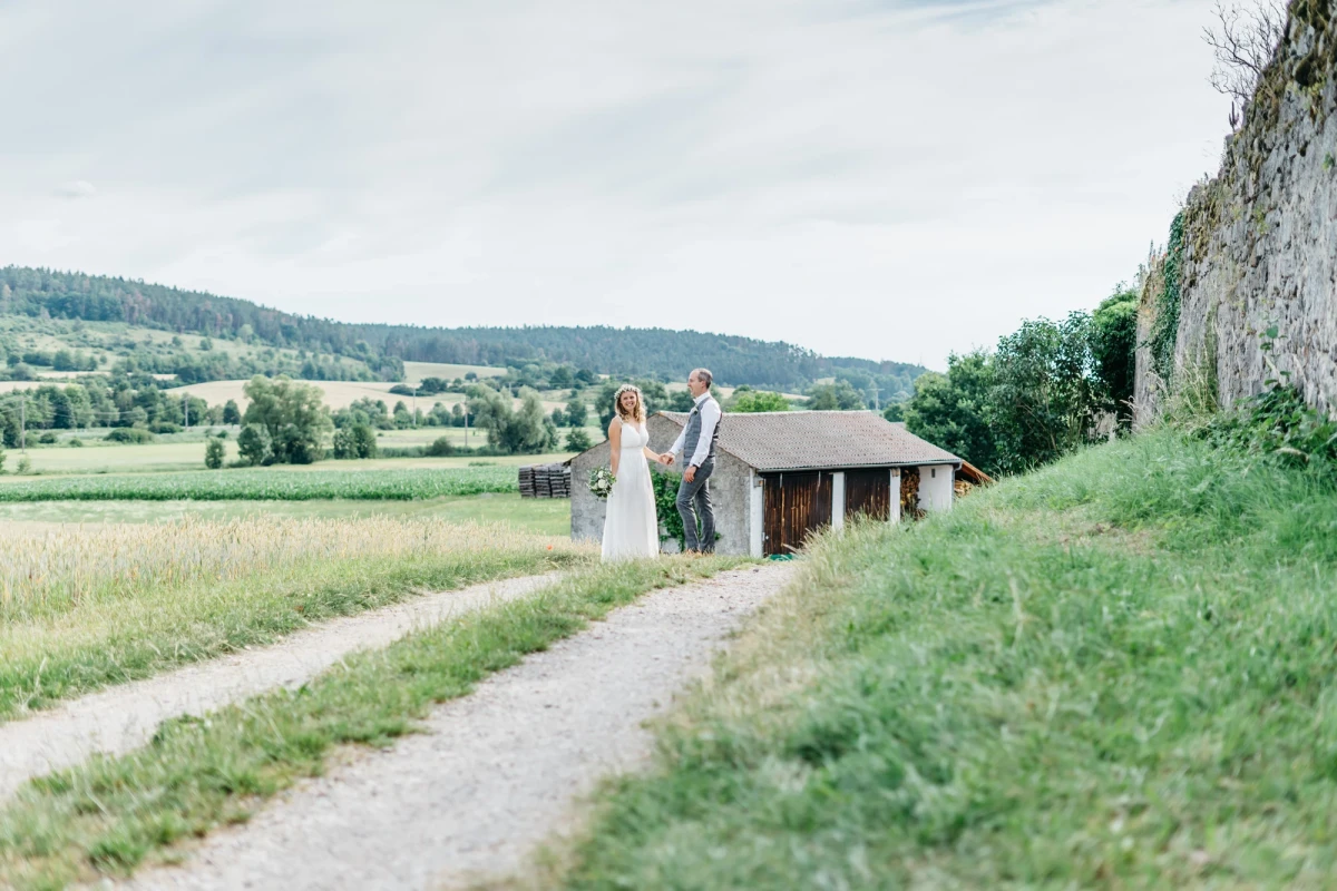 Brautpaar auf einem malerischen Weg vor l&auml;ndlicher Kulisse.